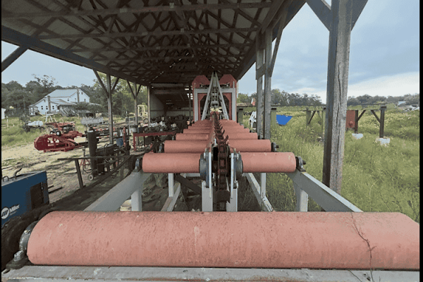 Heavy-duty Sharp Chain Scragg Mill with large rollers and conveyor system under a metal roof.