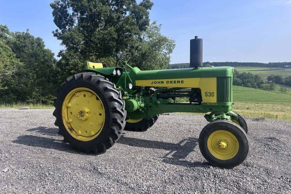 John Deere 530 vintage tractor with green body and yellow wheels on gravel surface.