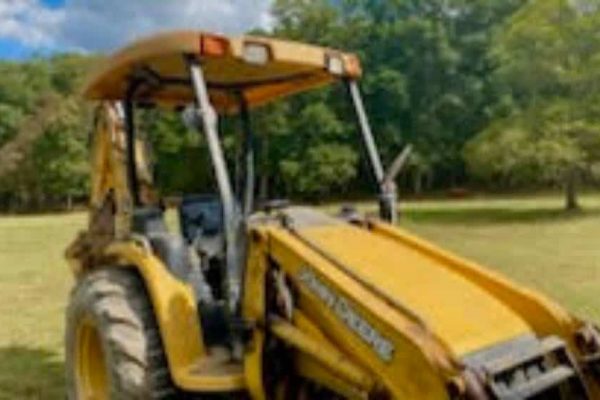 Yellow John Deere tractor with front loader attachment in a grassy field.