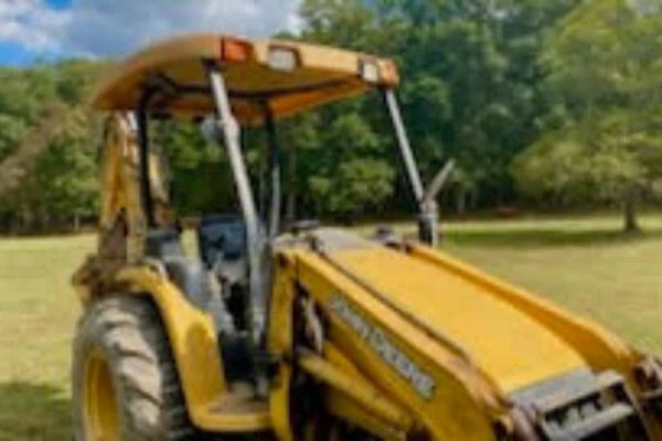 Yellow John Deere tractor with front loader attachment in a grassy field.